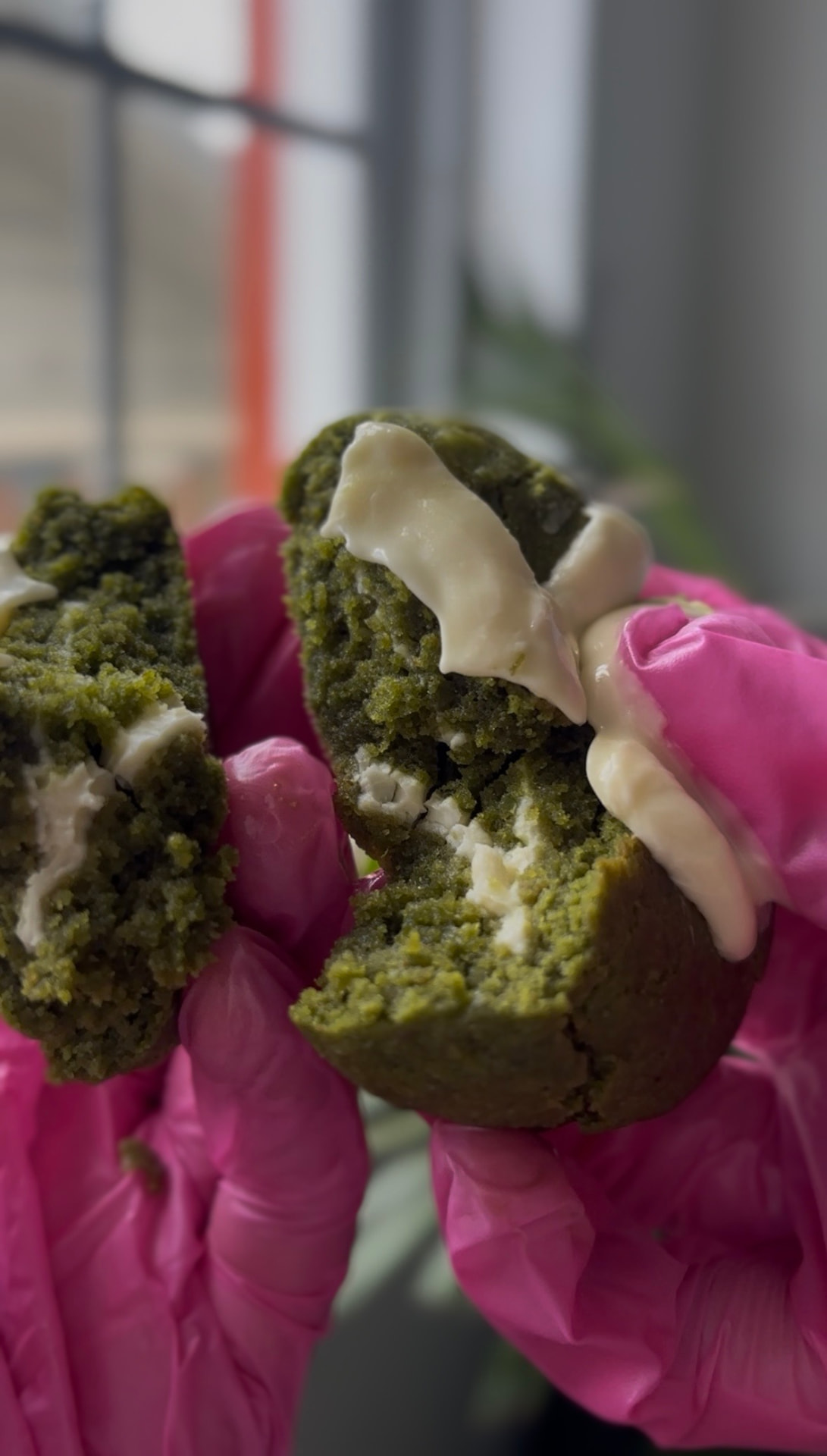 Matcha white chocolate cookie held in pink bakery gloves